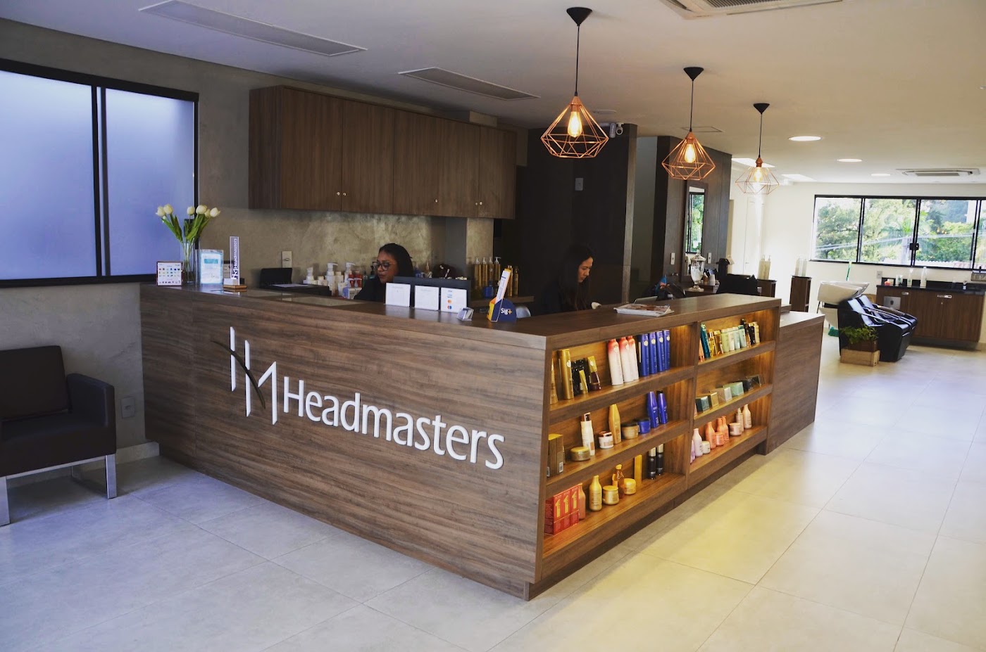 Recepção do Headmasters: balcão de madeira com o logo e luminárias de cobre