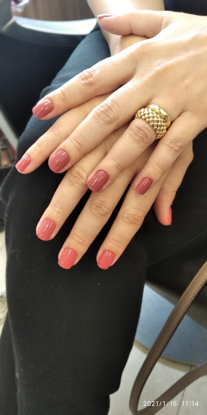 Unhas feitas com esmalte rosa e anéis dourados